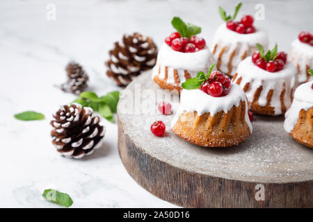 Small Christmas bundt cakes with sugar glaze and  currants on a rustic wood slice Stock Photo