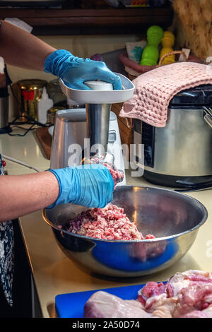 Cook makes minced fresh meat in a meat grinder. The process of grinding meat in a cafe. Stock Photo