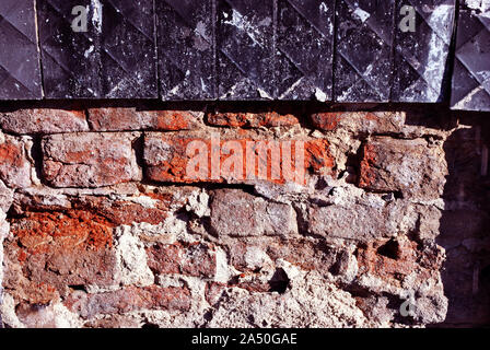Cracked black tile surface on red brick wall, grunge horizontal shabby background detail close up Stock Photo