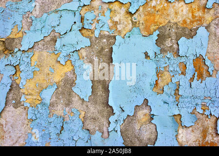 Cracked soft blue paint, plaster surface on yellow-gray wall, grunge horizontal shabby background detail close up Stock Photo