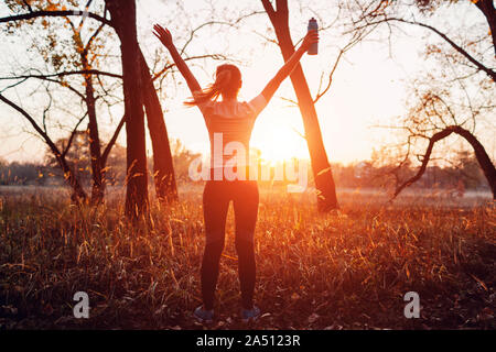 Runner raised arms after workout feeling free and happy succeeded in training. Woman admiring sunset. Healthy lifestyle Stock Photo