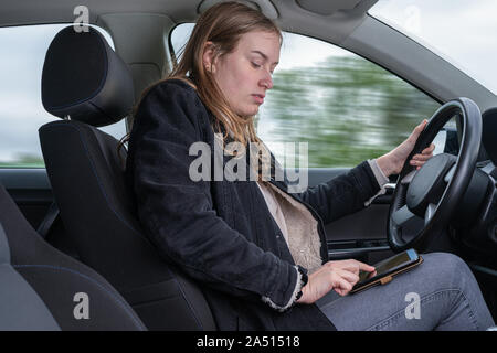 A young woman is typing on a mobile while driving a car and is distracted Stock Photo