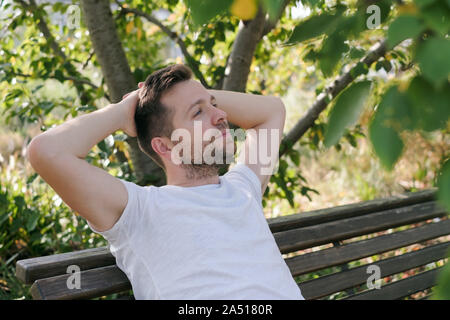 Young handsome guy dreaming about something sitting in city park. Student relaxing on a campus Stock Photo