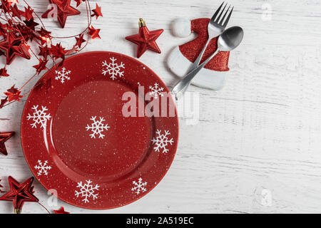 festive winter holiday place setting with snowflakes on red plate, star decor and santa hat with fork and spoon on a rustic white painted wood backgro Stock Photo