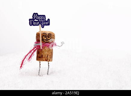 Funny wine cork manikin on white snow wishes anybody "happy new year". New Year composition with toys. Stock Photo