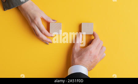 Male and female hand placing blank wooden blocks on bright yellow background. Stock Photo