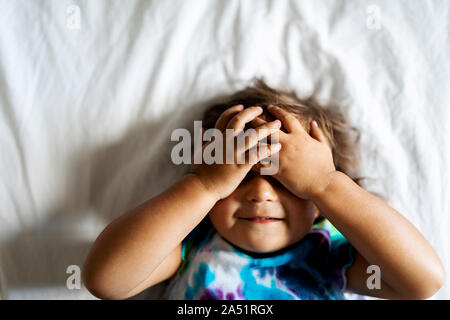 Toddler girl lying on the bed  and covering her eyes