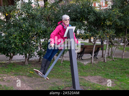 Senior woman enjoying using exercise equipment in public outdoor gym in city park Stock Photo