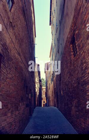 Vertical photo of very nice narrow street in famous Urbino town. The town is on UNESCO list. Buildings are on both sides built from ancient red bricks Stock Photo