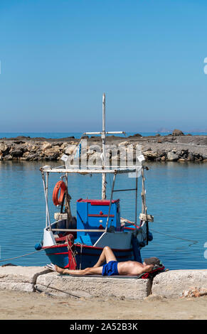 Gouves, Crete, Greece. October 2019.  Fisherman taking a nap next to his boat  at the small harbour at Kato Gouves a former US military base Stock Photo