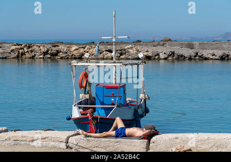 Gouves, Crete, Greece. October 2019.  Fisherman taking a nap next to his boat  at the small harbour at Kato Gouves a former US military base Stock Photo