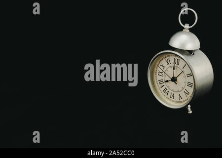 Classic and vintage matt gray alarm clock, marking eight o'clock, on a black background and slightly turned Stock Photo