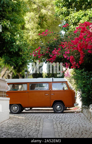 A Classic Orange And White VW Campervan Type 2 Third Generation Van Parked In A Picturesque Street With Flower Blossoms In Cascais Portugal Stock Photo