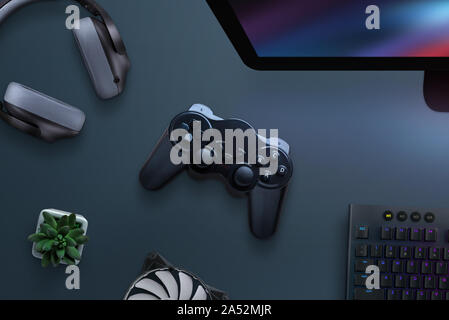 Joypad on desk surrounded with headphones, cooler, keyboard and computer display. PC gaming concept. Top view, flat lay. Stock Photo