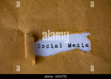 The text, social media, appears behind torn brown paper Stock Photo
