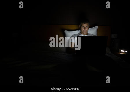 Man working on his laptop in the bed at night. Lifestyle concept Stock Photo