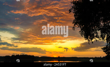 Beautiful scenic orange sunset into a cloud over a lake in late evening Stock Photo