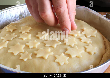 Traditional American homemade Christmas pie. Closeup of man's hands decorating an apple pie dessert with small short crust pastry stars Stock Photo