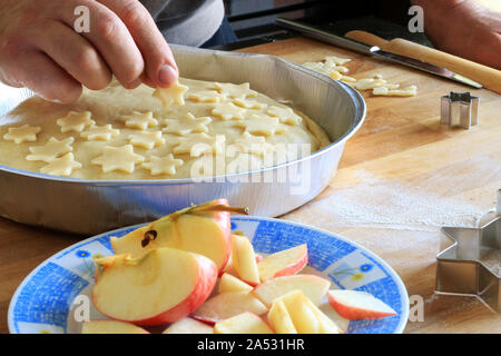 Traditional American homemade Christmas pie. Closeup of man's hands decorating an apple pie dessert with small short crust pastry stars Stock Photo