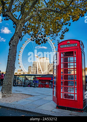 London, England, United Kingdom - October 05, 2019: London Eye and red traditional photo cabine on the riverbank of Thames river in autumn season Stock Photo