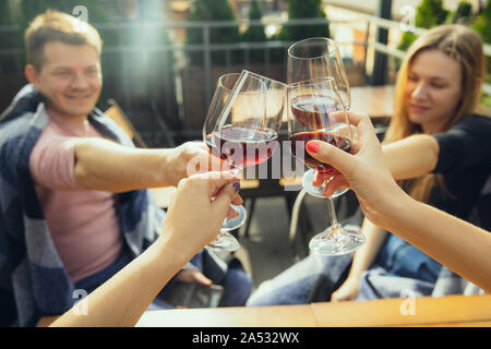 People clinking glasses with wine on the summer terrace of cafe or restaurant. Happy cheerful friends celebrate summer or autumn fest. Close up shot of human hands, lifestyle. Stock Photo