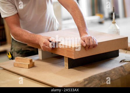 Carpenter sanding the edge of a wooden block with sand paper in a woodworking workshop in a close up on his hands Stock Photo
