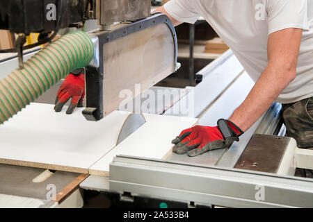 Carpenter or joiner cutting a wooden board with a circular saw in a woodworking workshop in a close up on his hands and the power tool Stock Photo