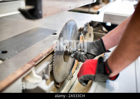 Carpenter adjusting the toothed round blade on a circular saw in a woodworking workshop in a close up on his gloved hands and the power tool Stock Photo