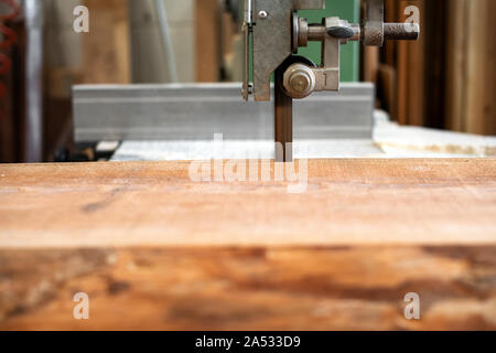 Sawing wood using a band saw in a woodworking or carpentry workshop in a close up on the wooden plank and the band of the saw Stock Photo