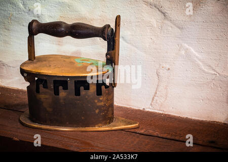 An old iron standing on a wooden countertop against a white wall in an old abandoned house. Stock Photo