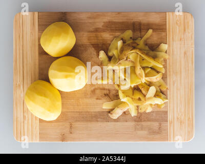 Potato peelings with potatoes on wooden cutting board on grey background. Top view. Stock Photo