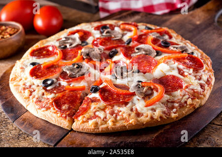 A brick oven baked pizza deluxe with pepperoni, mushroom, red pepper, onion and black olives or a rustic wood board. Stock Photo