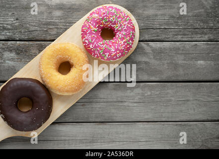 three donuts on a wooden board background with blank space Stock Photo