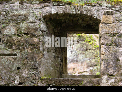 view through a window in the wall of the ruins of an old water mill made of natural stone in the forest near Dolny Mlyn in Bohemian Switzerland nation Stock Photo