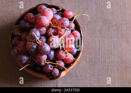 Ripe red grapes in a bowl isolated on brown background. Top view Stock Photo
