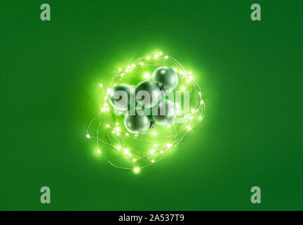 Green Christmas balls and lit Christmas lights on green background. Above view of Xmas ornaments. Flat lay with traditional decorations for Christmas Stock Photo