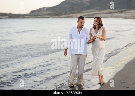 beautiful pregnant woman and her man walk on the beach on sunset Stock Photo