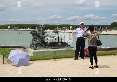 Versailles, Ile de France / France - June 21, 2016: Chinese tourists posing and taking photos in front of the bronze statue of King Neptune in a Versa Stock Photo