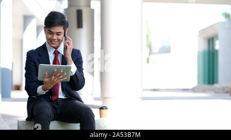 Young businessman in black suit speaking over mobile or smart phone with business partners. Business outdoors. Stock Photo