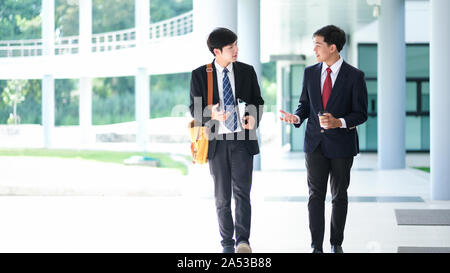 Business people walking and talking in the office building.  Two confident business partners walking down in office building and talking while taking Stock Photo