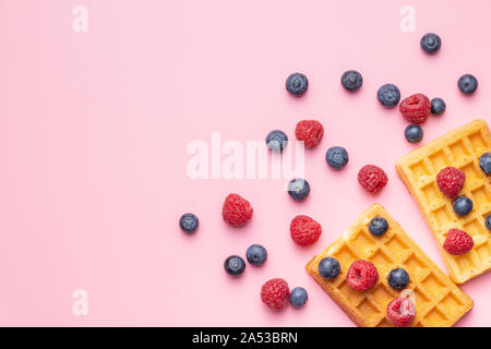 Waffles with blueberries and raspberries on pink background. Top view. Stock Photo