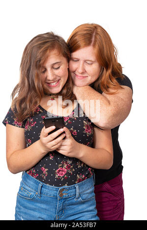 Vertical studio shot of a mother leaning on her daughter’s shoulder watching her use her cell phone.  They are both smiling.  White background. Stock Photo