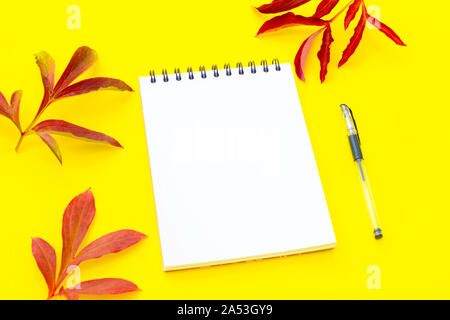 Open empty notebook with a pen on a yellow background with autumn leaves. Stock Photo