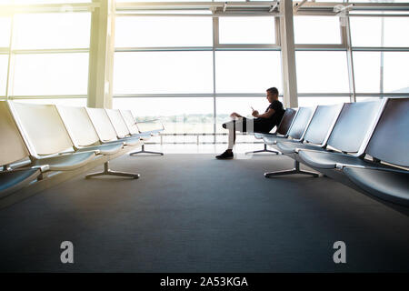 Portrait of young handsome man wearing casual style clothes sitting on the bench in modern airport terminal using smartphone. Traveler making call, me Stock Photo