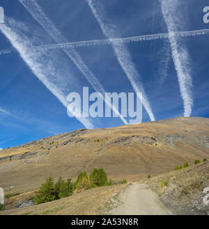 contrails (condensation trails) crossing, vapour trails made by jet in the sky above a mountain dirt road (symbol of chaotic air traffic ) Stock Photo