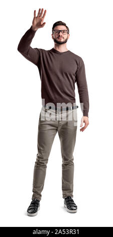 A young bearded man in cargo pants holds up his hand to touch something or to wave. Stock Photo