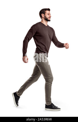 A young bearded man in a side view walks fast on the verge of running on a white background. Stock Photo