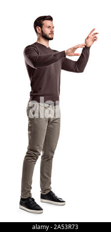 A young man in fashionable casual closes stands on a white background with hands as if pressing invisible buttons. Stock Photo