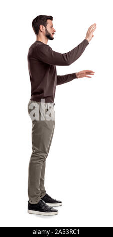 A bearded man in casual clothes stands still in a side view and used both hands to touch invisible digital screen. Stock Photo