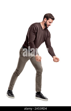 A fit bearded young man in casual clothes tries to pull an invisible rope with all his strength from low grip. Stock Photo
